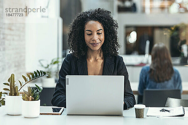 Lächelnde Geschäftsfrau benutzt Laptop am Schreibtisch am Arbeitsplatz