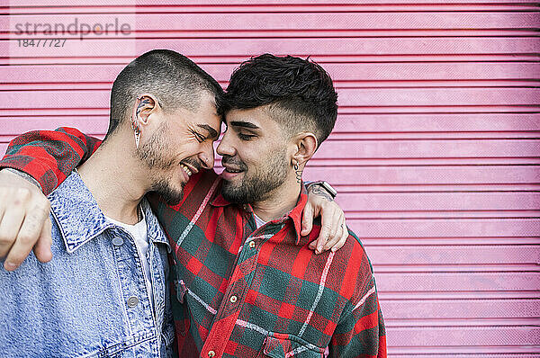 Gay couple standing with arms around each other in front of roller shutter wall