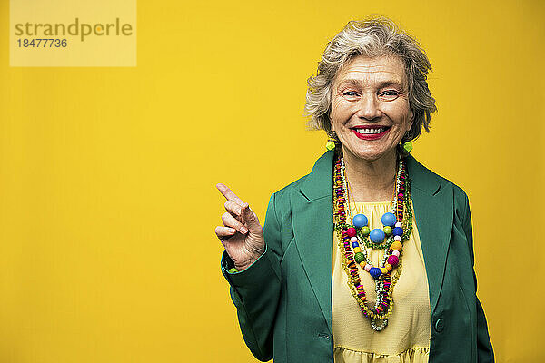 Lächelnde ältere Frau zeigt vor gelbem Hintergrund