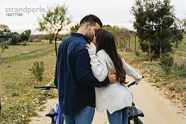 Romantic couple with bicycles kissing on dirt road