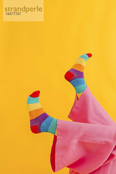 Füße einer Frau mit regenbogenfarbenen Socken auf gelbem Hintergrund