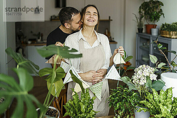 Man hugging woman from back by plants at home