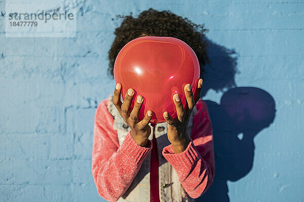 Junge Frau hält roten Ballon über Gesicht