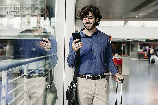 Glücklicher Geschäftsmann benutzt Smartphone am Bahnhof