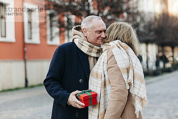Älterer Mann hält Geschenkbox in der Hand und steht mit Frau auf der Straße