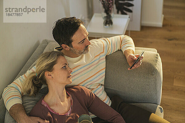 Mature man using mobile phone sitting with woman on sofa at home