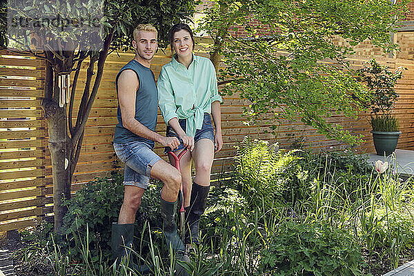 Glückliches junges Paar steht mit Schaufel im Garten