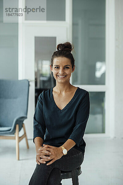 Lächelnde Geschäftsfrau  die im Heimbüro auf einem Hocker sitzt