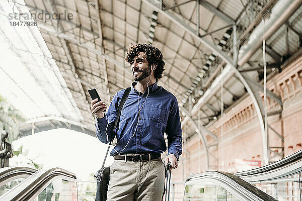 Glücklicher Geschäftsmann mit Smartphone  der auf der Rolltreppe steht