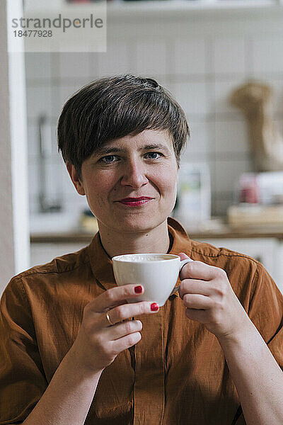 Lächelnde reife Frau hält Kaffeetasse zu Hause