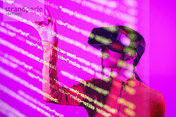 Frau mit VR-Brille berührt Computercodes auf rosa Hintergrund
