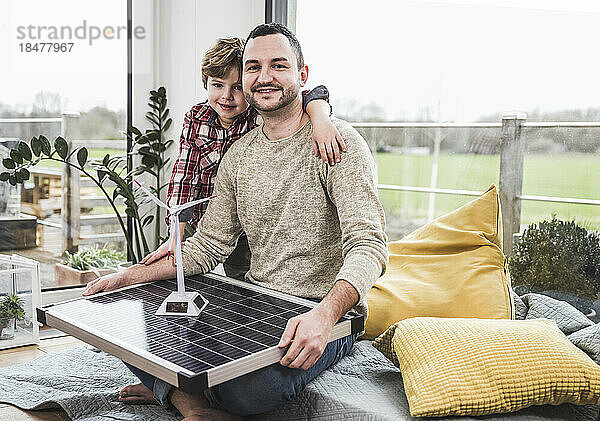 Lächelnder Mann mit Windkraftanlage und Solarpanel-Modell von Sohn zu Hause