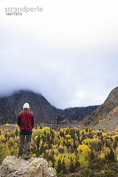 Mann steht auf einer Klippe und blickt auf die Berge