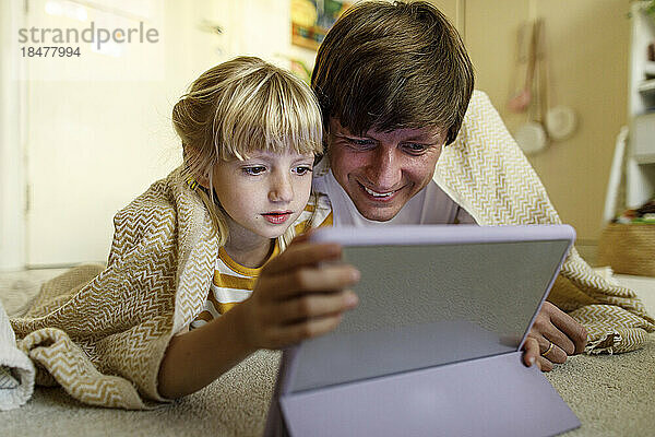 Vater und Tochter schauen zu Hause auf den Tablet-PC  der auf dem Boden liegt