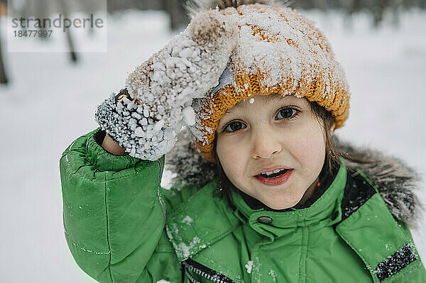 Unschuldiger Junge mit Strickmütze und schneebedeckten Handschuhen