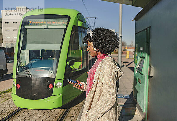 Frau benutzt Smartphone an Straßenbahnhaltestelle