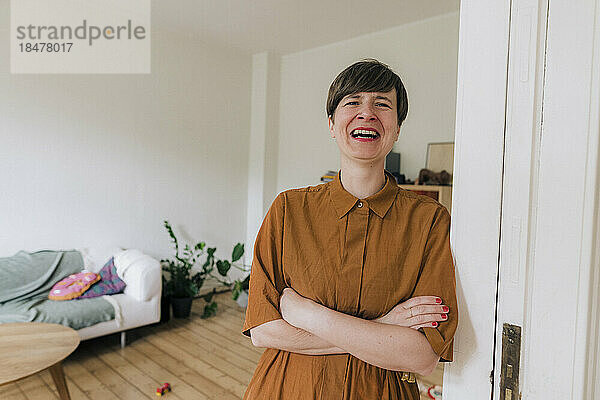 Happy woman with arms crossed leaning on doorway at home