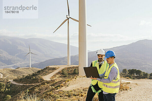 Techniker und Ingenieur arbeiten am Laptop vor Windkraftanlagen