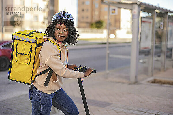 Lächelnde Lieferfrau mit Elektroroller am Fußweg