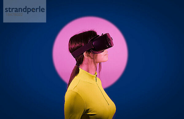 Frau schaut mit einer Virtual-Reality-Brille bei rosafarbenem Licht auf schwarzem Hintergrund zu