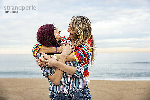 Frau umarmt Freundin von hinten am Strand