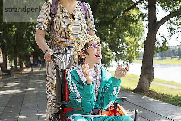 Mädchen mit Behinderung sitzt im Rollstuhl und genießt mit Mutter den Gehweg
