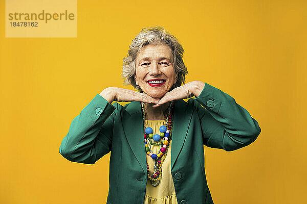 Happy senior woman standing against yellow background
