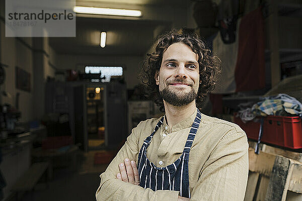 Contemplative businessman wearing apron with arms crossed in storage room