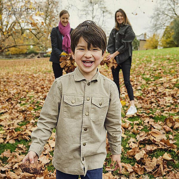 Fröhlicher Junge steht auf Herbstblättern im Park
