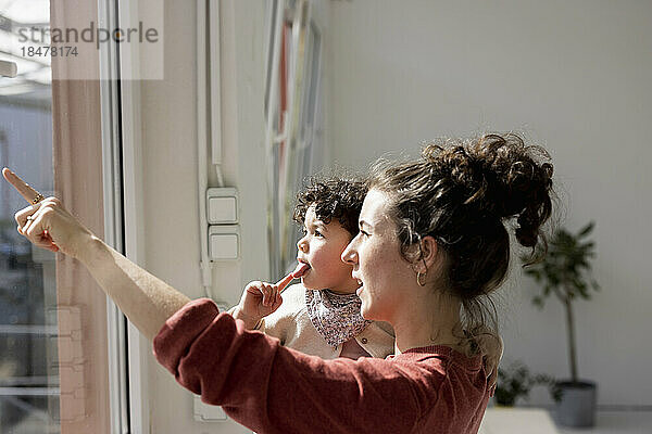 Mother carrying daughter pointing out of window