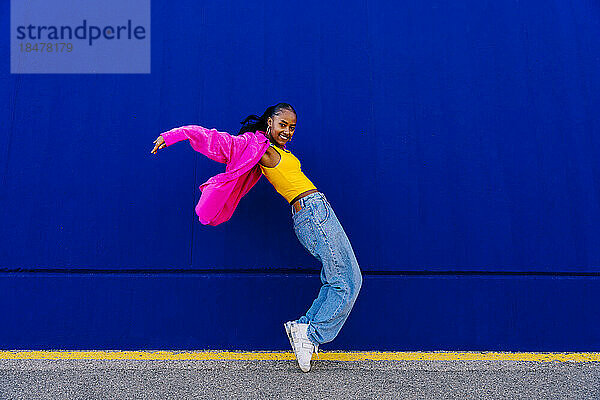 Glückliche Frau tanzt auf Zehenspitzen an der blauen Wand