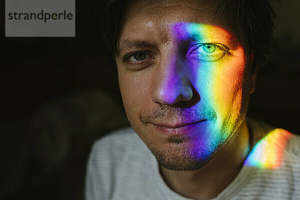 Lächelnder Mann mit Regenbogenlicht im Gesicht