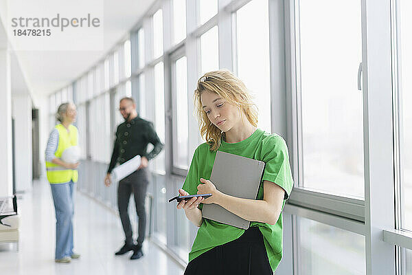 Woman using mobile phone on office floor with colleagues in background