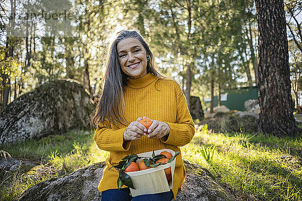 Lächelnde reife Frau hält Kiste mit Mandarinen