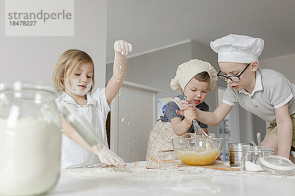 Mädchen bereitet Teig zu  während Brüder zu Hause Eier in einer Schüssel mischen