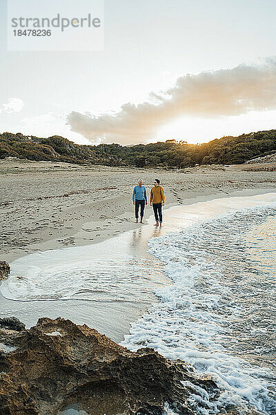 Mann steht mit Vater bei Sonnenuntergang an der Küste