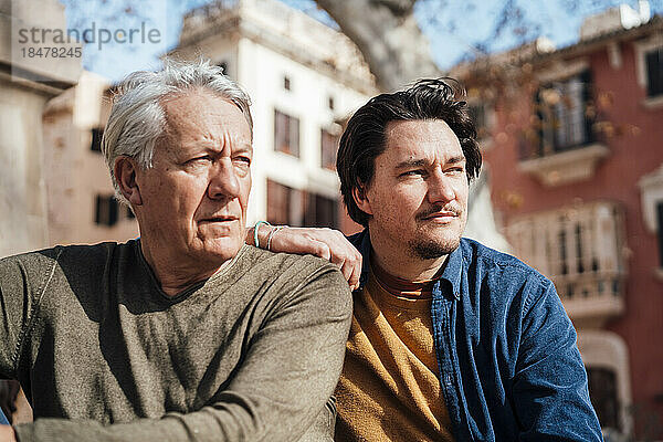 Nachdenklicher älterer Mann sitzt mit Sohn vor dem Gebäude