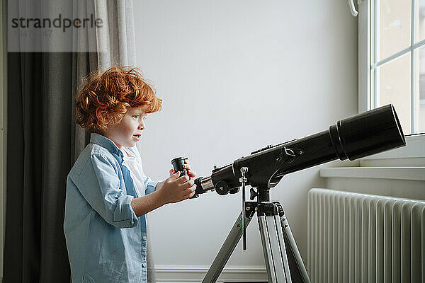 Junge steht zu Hause neben dem Teleskop