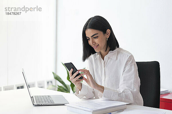 Lächelnde Geschäftsfrau benutzt Mobiltelefon am Schreibtisch