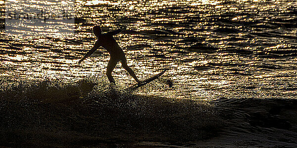 Silhouette eines Mannes  der bei Sonnenuntergang auf dem Meer surft  Pembrokeshire  Wales