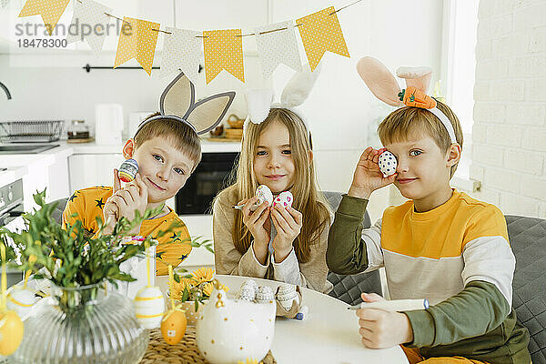 Happy boys and girl wearing rabbit ears headbands and holding Easter eggs at home