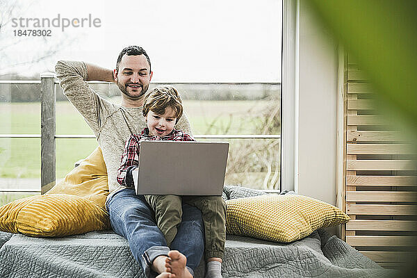 Lächelnder Vater und Sohn schauen zu Hause gemeinsam auf den Laptop