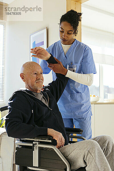 Physiotherapeut hilft älterem Mann im Rollstuhl beim Training zu Hause