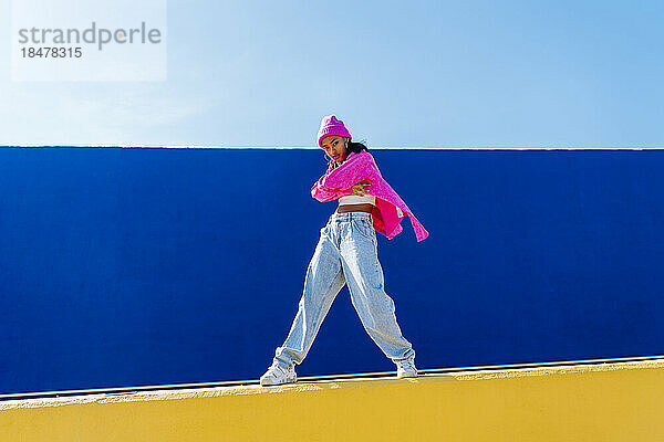 Junge Frau mit rosa Strickmütze steht an der Wand