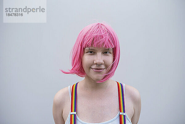 Lächelnde nicht-binäre Person mit rosa Perücke vor der Wand
