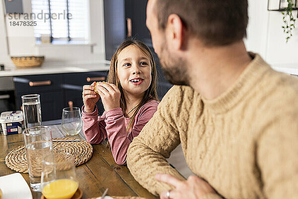 Glückliches Mädchen beim Frühstück mit Vater  der in der Küche sitzt