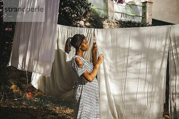 Schwangere Frau hängt weißes Laken im Hinterhof auf