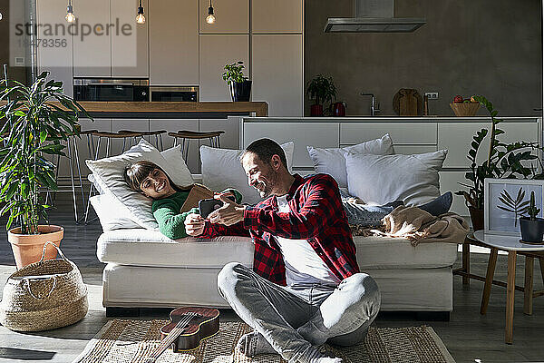 Mann teilt Smartphone mit Frau  die zu Hause auf der Couch liegt