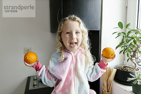 Glückliches Mädchen hält Orangen in der heimischen Küche