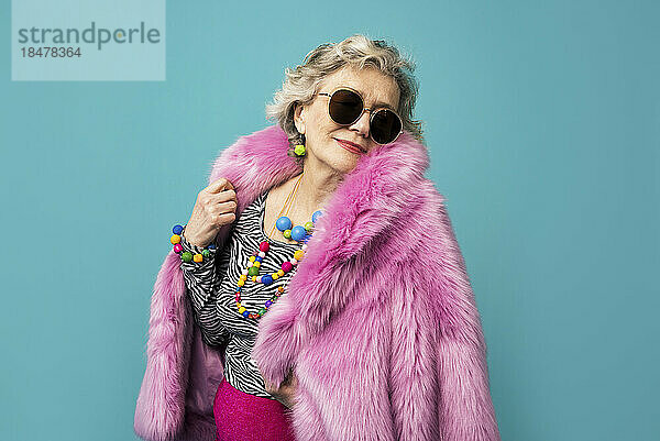 Cool senior woman wearing pink fur coat against colored background
